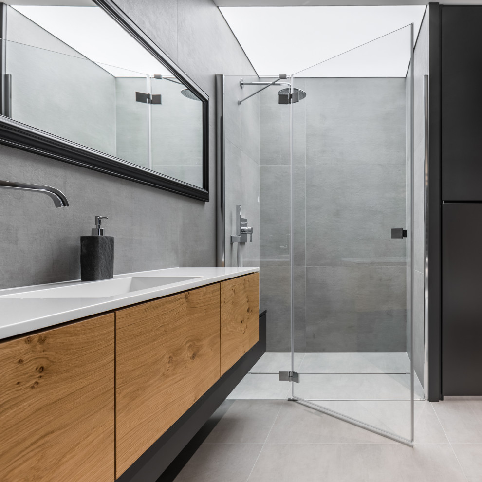 Walk-in shower - mid-sized modern master gray tile and ceramic tile porcelain tile and gray floor walk-in shower idea in Malaga with flat-panel cabinets, brown cabinets, a wall-mount toilet, gray walls, a trough sink, quartz countertops, a hinged shower door and white countertops