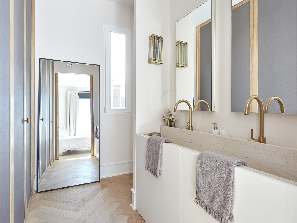 Modern inredning av ett badrum, med släta luckor, vita skåp, vita väggar, ljust trägolv, ett avlångt handfat och beiget golv
