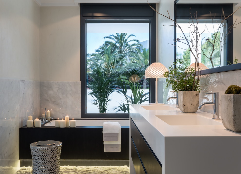 Example of a mid-sized trendy master black and white tile and stone slab alcove bathtub design in Madrid with flat-panel cabinets, black cabinets, white walls, an integrated sink and solid surface countertops