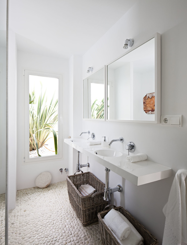 Ejemplo de cuarto de baño mediterráneo de tamaño medio con paredes blancas, suelo de baldosas tipo guijarro, aseo y ducha, lavabo suspendido, encimera de acrílico y espejo con luz