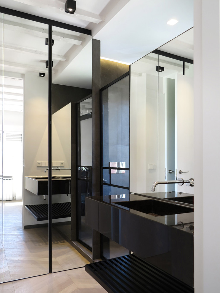 Photo of a modern wet room bathroom in Madrid with open cabinets, dark wood cabinets, a wall mounted toilet, white walls, light hardwood flooring, a submerged sink, engineered stone worktops, a hinged door and black worktops.