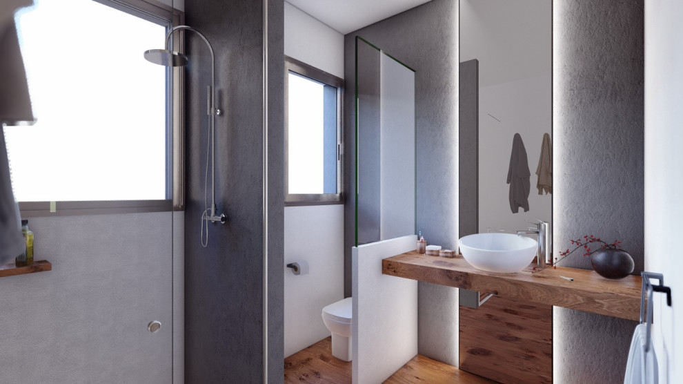 Foto på ett mellanstort funkis brun badrum med dusch, med öppna hyllor, vita skåp, en kantlös dusch, en toalettstol med hel cisternkåpa, grå kakel, keramikplattor, grå väggar, laminatgolv, ett fristående handfat, träbänkskiva, brunt golv och dusch med gångjärnsdörr