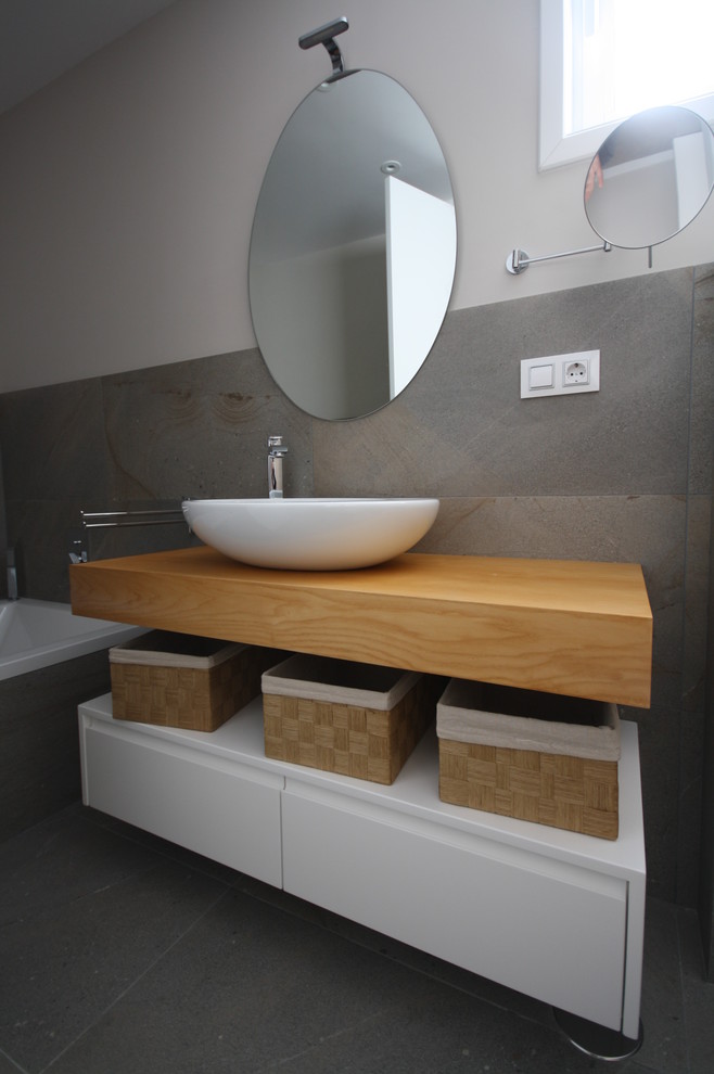 Идея дизайна: главная ванная комната среднего размера в скандинавском стиле с светлыми деревянными фасадами, биде, серой плиткой, керамической плиткой, серыми стенами, полом из керамической плитки, настольной раковиной и столешницей из дерева