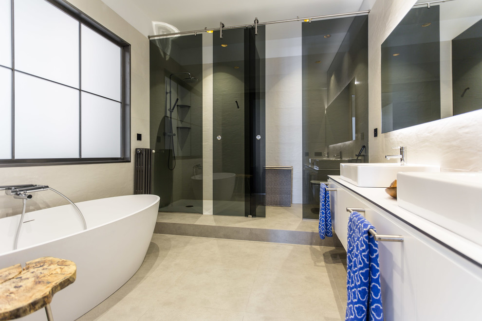 Стильный дизайн: большая главная ванная комната в современном стиле с плоскими фасадами, белыми фасадами, отдельно стоящей ванной, душем в нише, раздельным унитазом, белыми стенами, полом из керамической плитки и настольной раковиной - последний тренд