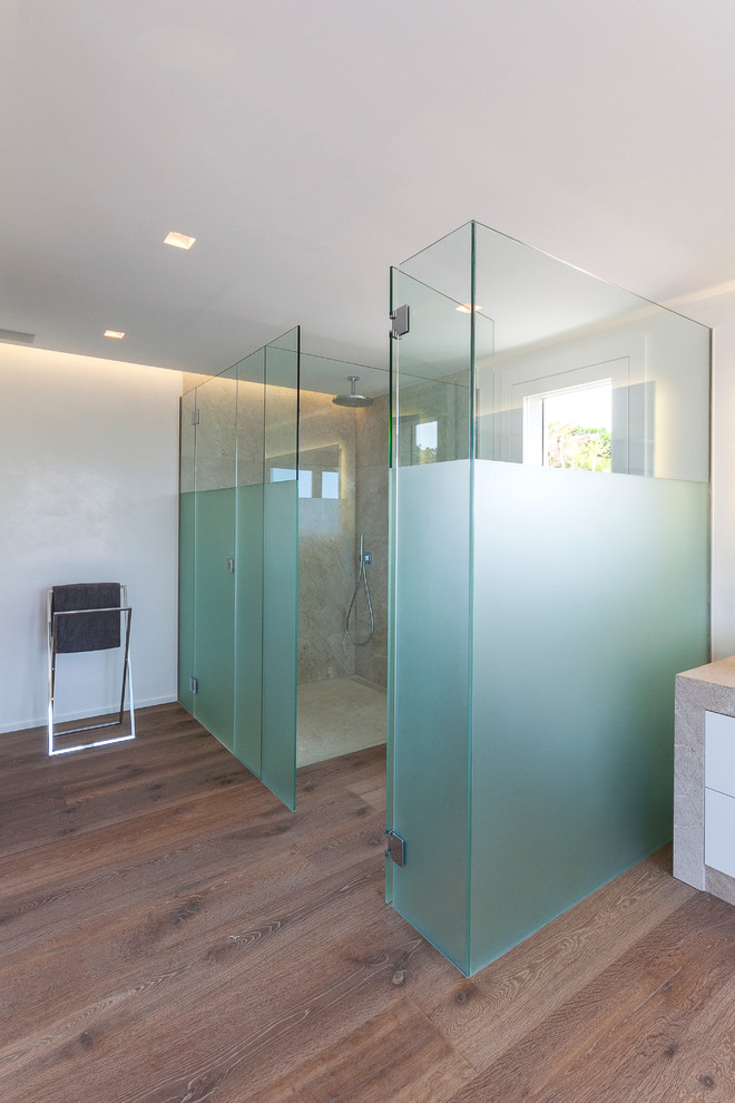 Modern inredning av ett stort en-suite badrum, med släta luckor, vita skåp, en kantlös dusch, en vägghängd toalettstol, beige kakel, vita väggar, mellanmörkt trägolv och bänkskiva i kalksten