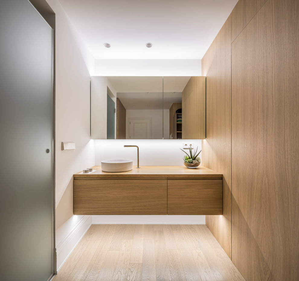 Modern inredning av ett mellanstort badrum, med vita väggar, ett fristående handfat, träbänkskiva, beiget golv, släta luckor, skåp i ljust trä och ljust trägolv