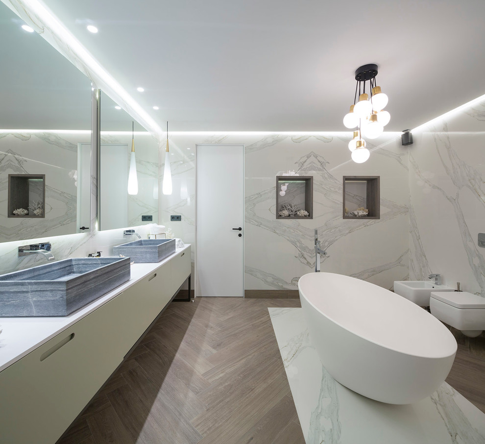 Idée de décoration pour une grande salle de bain principale design avec un placard à porte plane, des portes de placard blanches, une baignoire indépendante, un bidet, un mur blanc et une vasque.