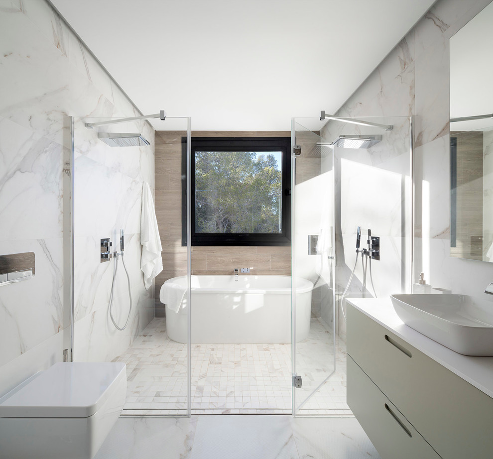 Inredning av ett modernt en-suite badrum, med släta luckor, gröna skåp, ett fristående badkar, en dubbeldusch, en vägghängd toalettstol, vit kakel, vita väggar, ett avlångt handfat och dusch med gångjärnsdörr