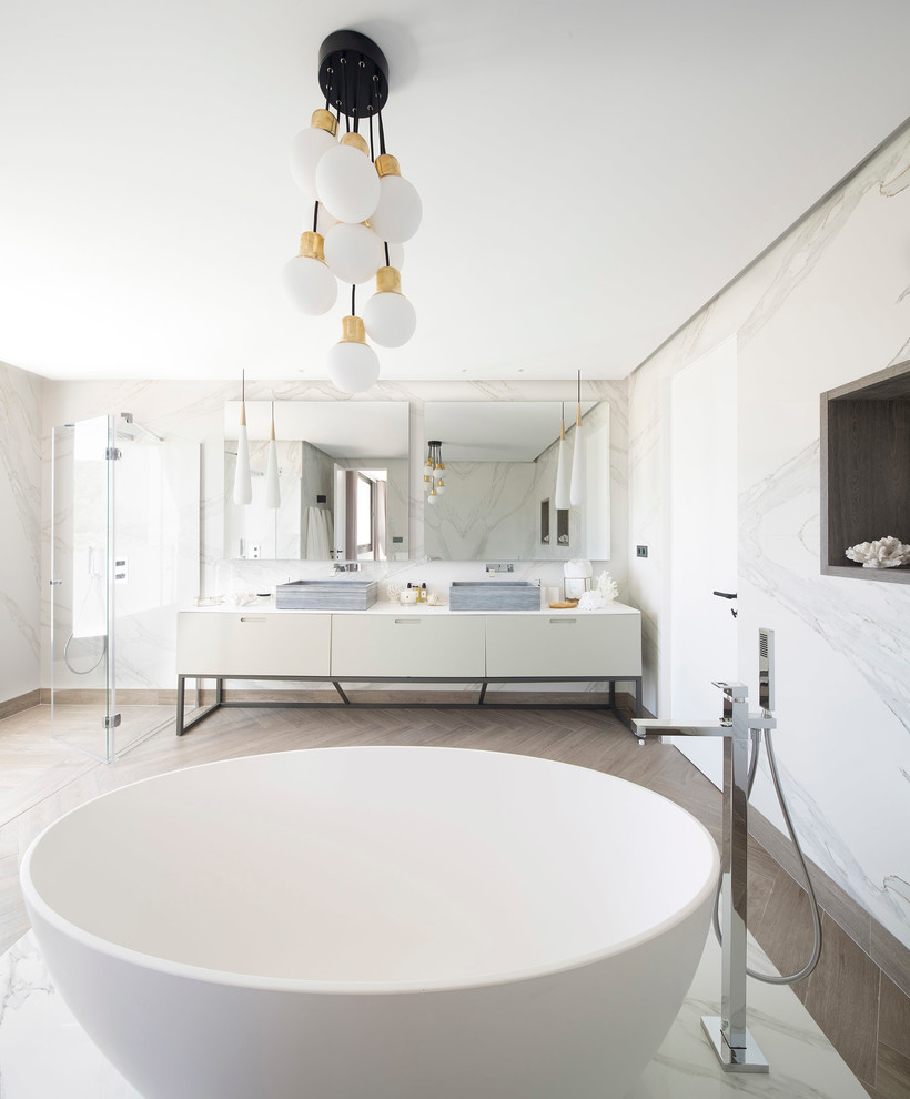 Geräumiges Modernes Badezimmer En Suite mit flächenbündigen Schrankfronten, weißen Schränken, freistehender Badewanne, bodengleicher Dusche, weißer Wandfarbe, Aufsatzwaschbecken und Falttür-Duschabtrennung in Bilbao