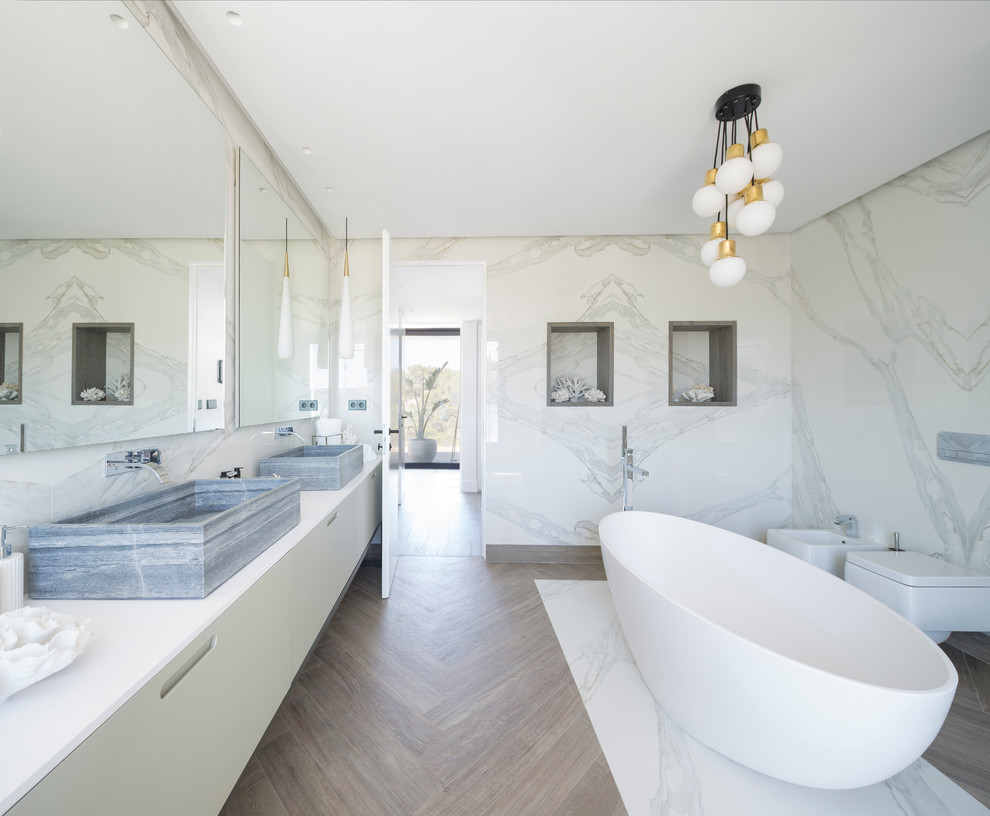 Geräumiges Modernes Badezimmer En Suite mit flächenbündigen Schrankfronten, weißen Schränken, freistehender Badewanne, Duschbadewanne, Bidet, beiger Wandfarbe und Aufsatzwaschbecken in Bilbao
