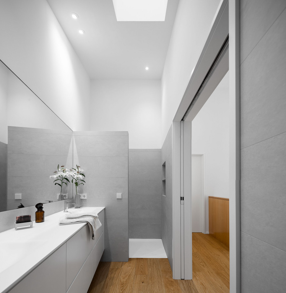 Foto på ett funkis vit badrum, med släta luckor, grå skåp, en kantlös dusch, vita väggar, mellanmörkt trägolv, ett integrerad handfat, brunt golv och med dusch som är öppen