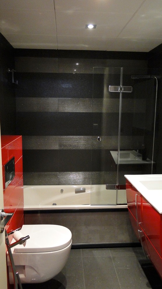 Réalisation d'une salle de bain principale design de taille moyenne avec un placard à porte plane, des portes de placard rouges, une baignoire en alcôve, un combiné douche/baignoire, WC suspendus, un mur noir et un lavabo intégré.