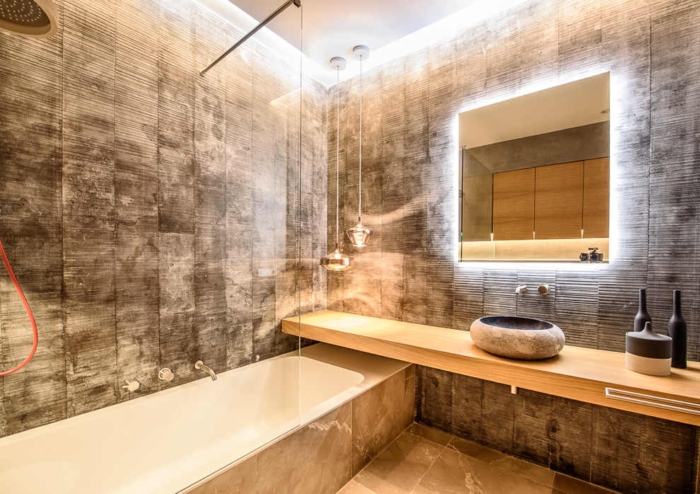 Foto de cuarto de baño principal moderno grande con puertas de armario de madera clara, bañera empotrada, baldosas y/o azulejos grises, suelo de piedra caliza, encimera de madera y suelo beige