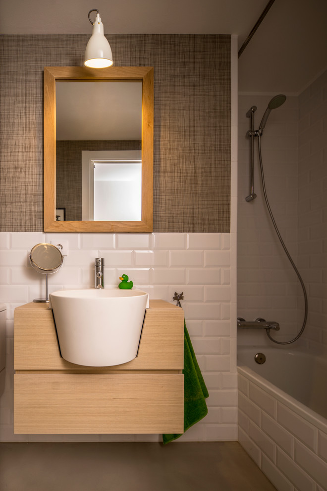 На фото: главная ванная комната среднего размера в скандинавском стиле с плоскими фасадами, светлыми деревянными фасадами, ванной в нише, душем над ванной, белыми стенами, бетонным полом и накладной раковиной с