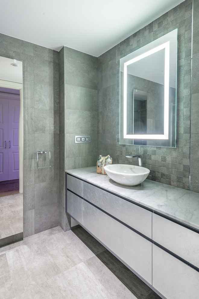 Réalisation d'une salle de bain principale design avec un carrelage gris, une vasque, un sol gris, un placard à porte plane, des portes de placard grises, des carreaux de béton, un mur gris, sol en béton ciré, un plan de toilette en marbre et un plan de toilette gris.