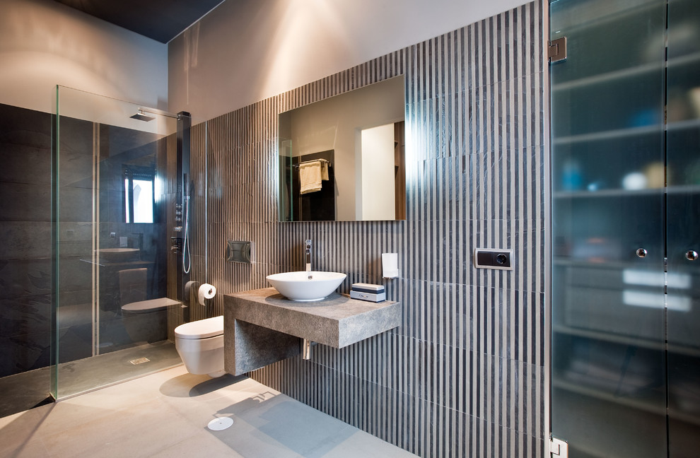 Diseño de cuarto de baño contemporáneo con ducha a ras de suelo, aseo y ducha, lavabo sobreencimera, sanitario de pared, baldosas y/o azulejos blancas y negros, paredes grises, suelo gris, ducha abierta y encimeras grises