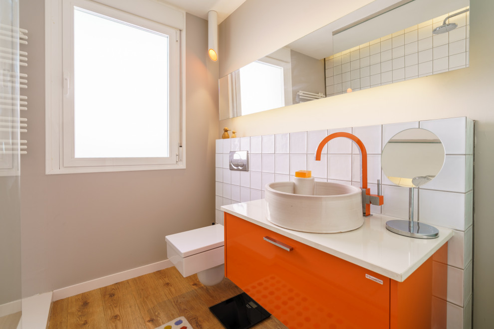 Modernes Duschbad mit flächenbündigen Schrankfronten, orangefarbenen Schränken, Duschnische, Wandtoilette, weißen Fliesen, beiger Wandfarbe, hellem Holzboden, Aufsatzwaschbecken, beigem Boden und weißer Waschtischplatte in Sonstige