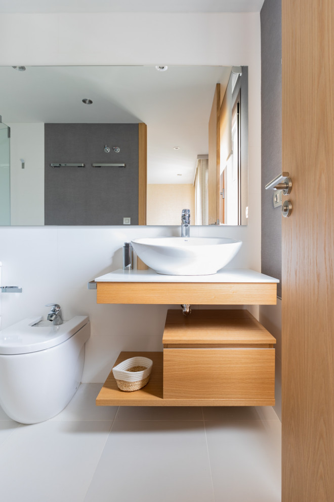 На фото: ванная комната в современном стиле с плоскими фасадами, светлыми деревянными фасадами, инсталляцией, белыми стенами, настольной раковиной, серым полом и белой столешницей