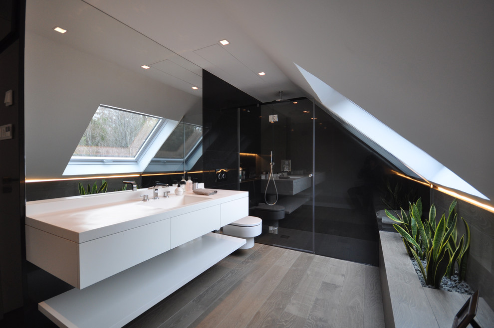 Réalisation d'une salle de bain design de taille moyenne avec un placard à porte plane, des portes de placard blanches, WC suspendus, un mur blanc, un lavabo intégré, un plan de toilette en surface solide et un sol en bois brun.