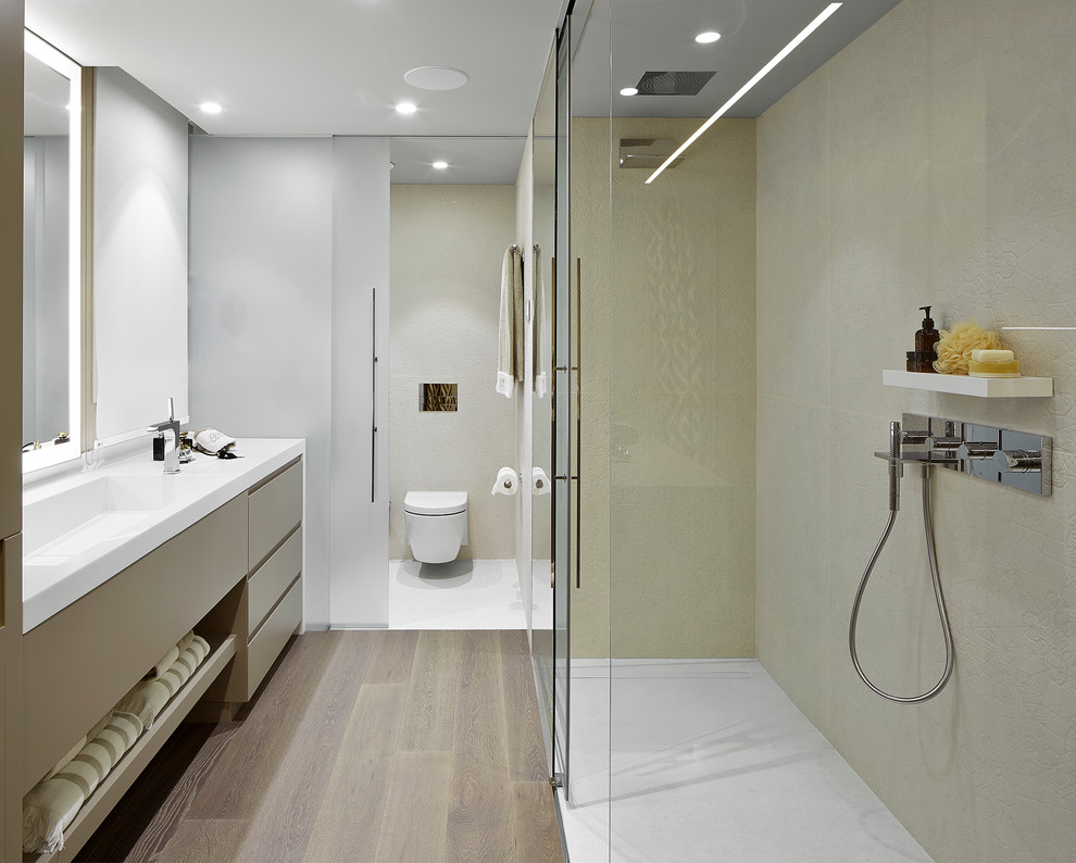 На фото: ванная комната среднего размера в современном стиле с плоскими фасадами, душем без бортиков, инсталляцией, душевой кабиной, монолитной раковиной, светлыми деревянными фасадами, бежевой плиткой, светлым паркетным полом и душем с раздвижными дверями