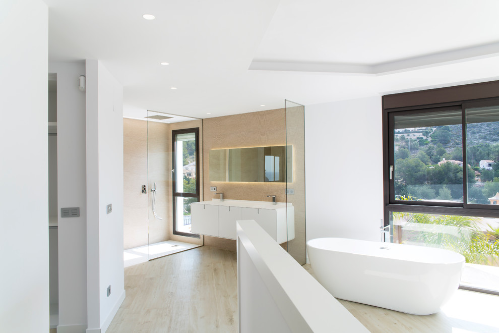 This is an example of an expansive contemporary ensuite bathroom in Other with flat-panel cabinets, white cabinets, a freestanding bath, a built-in shower, white walls, light hardwood flooring, an integrated sink, beige floors and a hinged door.