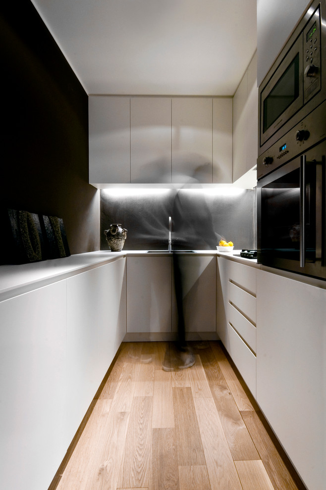Aménagement d'une petite cuisine contemporaine en U avec un placard à porte plane, des portes de placard blanches, une crédence noire, un électroménager en acier inoxydable et parquet clair.