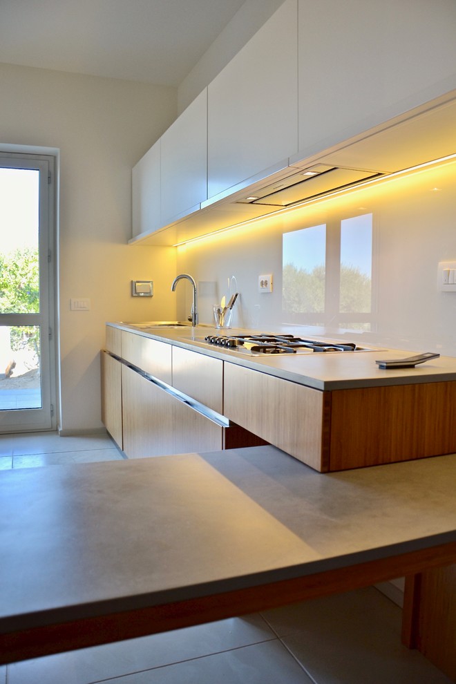 ローマにある高級な広いコンテンポラリースタイルのおしゃれなキッチン (ドロップインシンク、フラットパネル扉のキャビネット、白いキャビネット、コンクリートカウンター、白いキッチンパネル、ガラス板のキッチンパネル、シルバーの調理設備、コンクリートの床、白い床) の写真