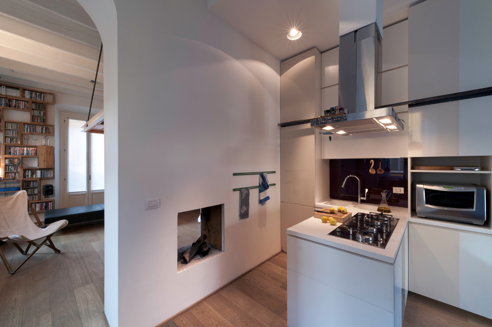 Medium sized contemporary l-shaped kitchen/diner in Milan with an integrated sink, flat-panel cabinets, white cabinets, composite countertops, red splashback, glass sheet splashback, stainless steel appliances, light hardwood flooring, a breakfast bar and beige floors.