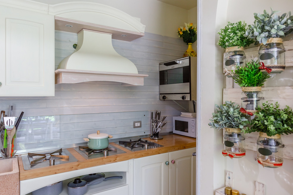 Shabby-Look Küche mit profilierten Schrankfronten, weißen Schränken, Arbeitsplatte aus Holz und Glasrückwand in Sonstige