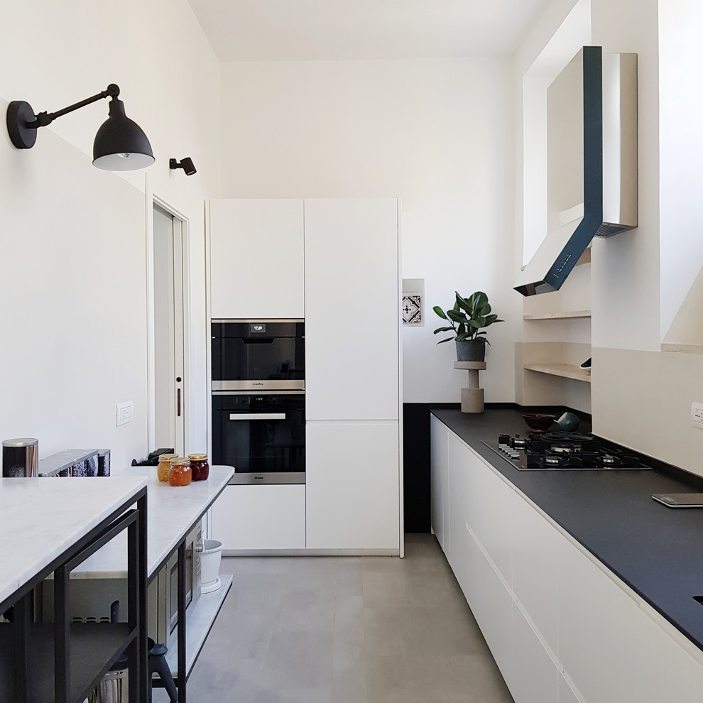 Diseño de cocina escandinava cerrada con armarios con paneles lisos, salpicadero beige, electrodomésticos negros, suelo de cemento, suelo gris, encimeras negras y con blanco y negro