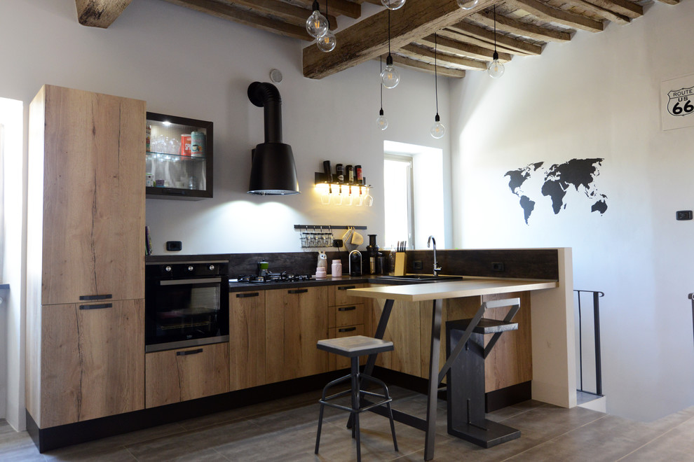 This is an example of an industrial kitchen in Florence with flat-panel cabinets, stainless steel appliances and brown floors.