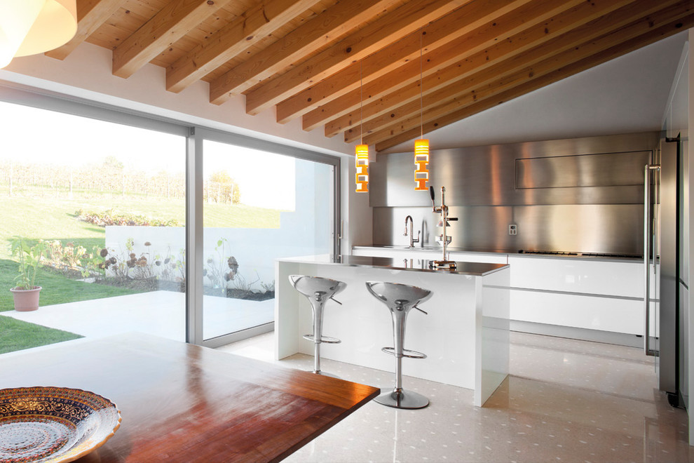 Exempel på ett mellanstort medelhavsstil kök, med en integrerad diskho, släta luckor, bänkskiva i rostfritt stål, stänkskydd med metallisk yta, stänkskydd i metallkakel, rostfria vitvaror, klinkergolv i porslin, en köksö och beiget golv