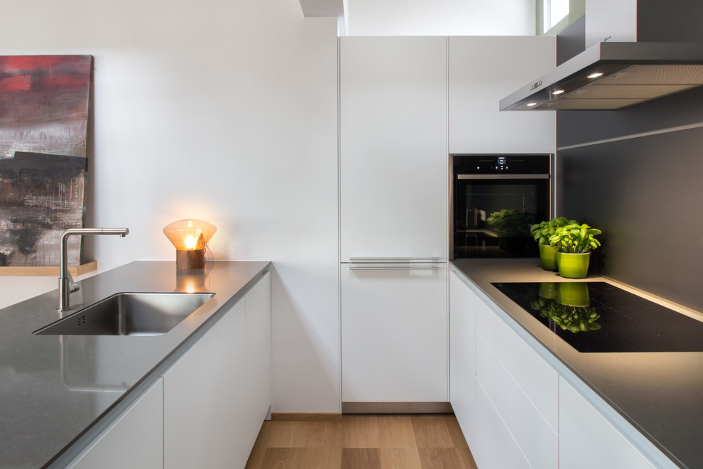 Photo of a large contemporary u-shaped open plan kitchen in Milan with a submerged sink, flat-panel cabinets, white cabinets, grey splashback, black appliances, medium hardwood flooring and a breakfast bar.