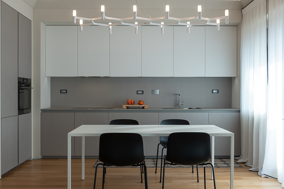 Photo of a contemporary l-shaped kitchen/diner in Turin with a built-in sink, flat-panel cabinets, grey cabinets, grey splashback, stone slab splashback, integrated appliances, light hardwood flooring, no island, beige floors and grey worktops.