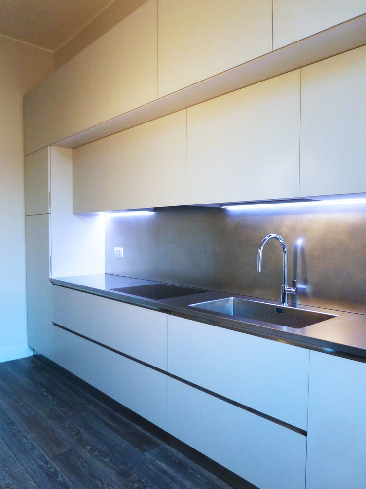 Zweizeilige, Mittelgroße Moderne Wohnküche mit integriertem Waschbecken, flächenbündigen Schrankfronten, weißen Schränken, Edelstahl-Arbeitsplatte, Küchenrückwand in Metallic, braunem Holzboden und grauem Boden in Mailand