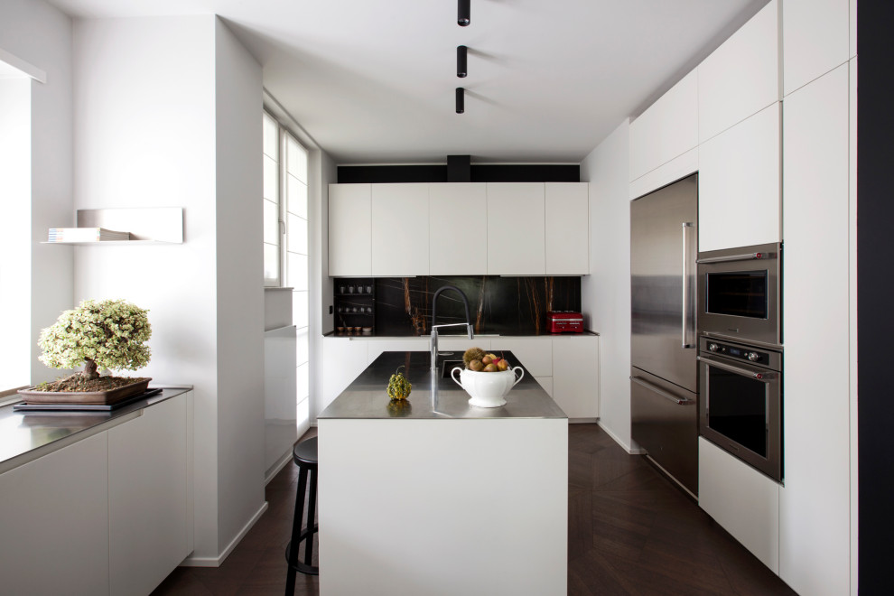 Foto på ett funkis svart l-kök, med en undermonterad diskho, släta luckor, vita skåp, svart stänkskydd, rostfria vitvaror, mörkt trägolv, en köksö och brunt golv
