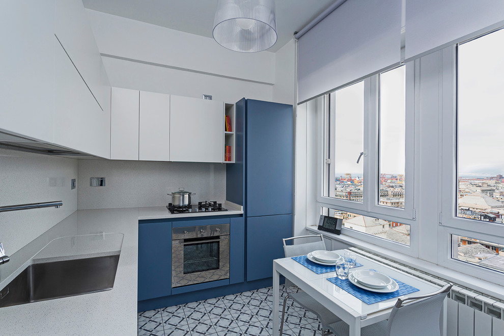 Пример оригинального дизайна: отдельная, угловая кухня среднего размера в современном стиле с врезной мойкой, плоскими фасадами, синими фасадами, серым фартуком, техникой из нержавеющей стали и синим полом без острова