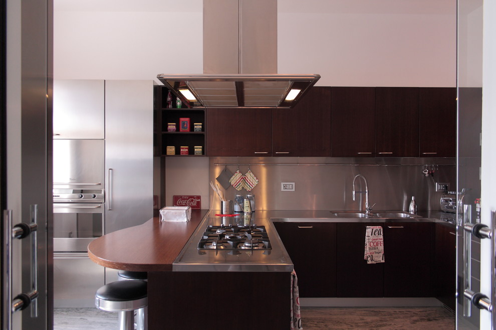 Immagine di una grande cucina ad U minimalista chiusa con lavello a doppia vasca, ante lisce, ante in legno bruno, top in acciaio inossidabile e penisola