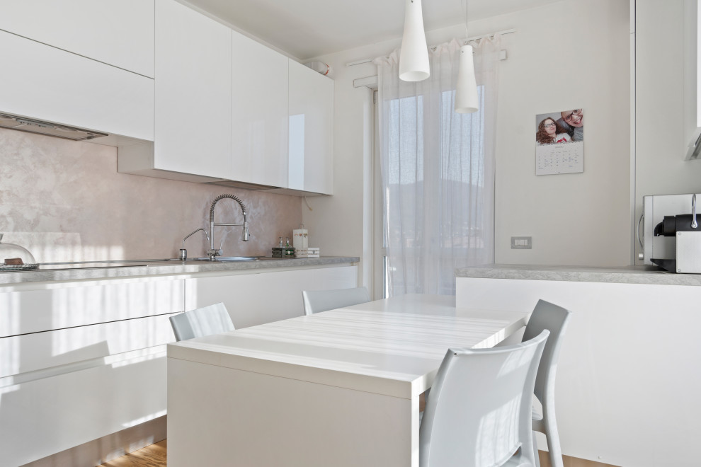 This is an example of a medium sized modern enclosed kitchen in Milan with a built-in sink, flat-panel cabinets, white cabinets, laminate countertops, stainless steel appliances, light hardwood flooring, a breakfast bar and grey worktops.