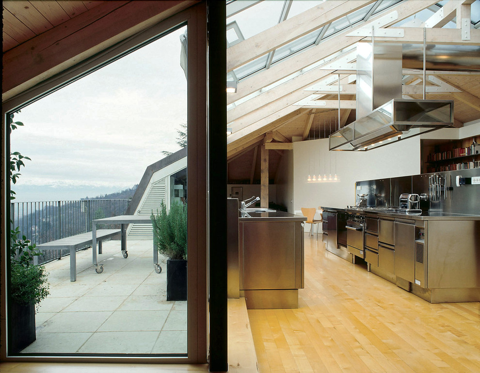 Bild på ett mycket stort funkis kök, med en enkel diskho, släta luckor, skåp i rostfritt stål, bänkskiva i rostfritt stål, rostfria vitvaror, ljust trägolv, flera köksöar och stänkskydd med metallisk yta