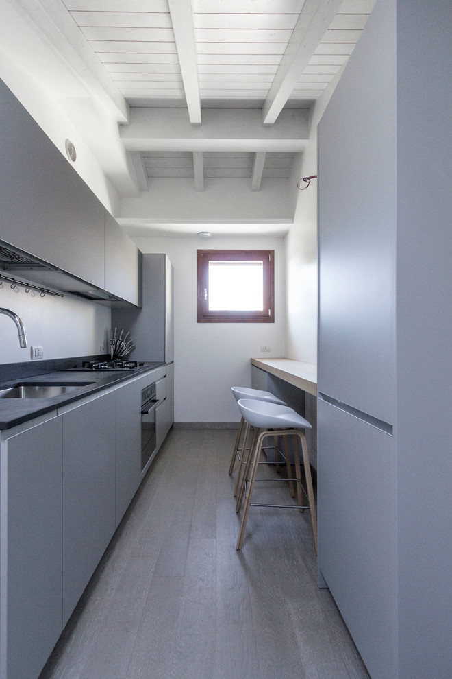 Zweizeilige, Kleine Moderne Schmale Küche ohne Insel mit Unterbauwaschbecken, flächenbündigen Schrankfronten, grauen Schränken, Küchengeräten aus Edelstahl und dunklem Holzboden in Mailand