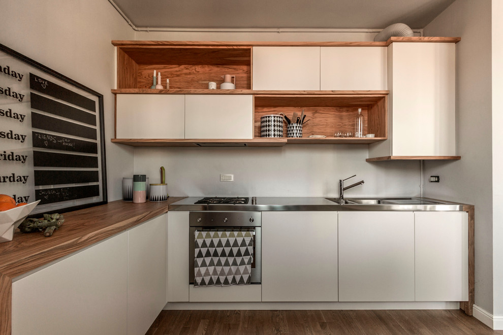Moderne Küche in L-Form mit integriertem Waschbecken, flächenbündigen Schrankfronten, weißen Schränken, Edelstahl-Arbeitsplatte, Küchenrückwand in Weiß, Küchengeräten aus Edelstahl und braunem Holzboden in Mailand