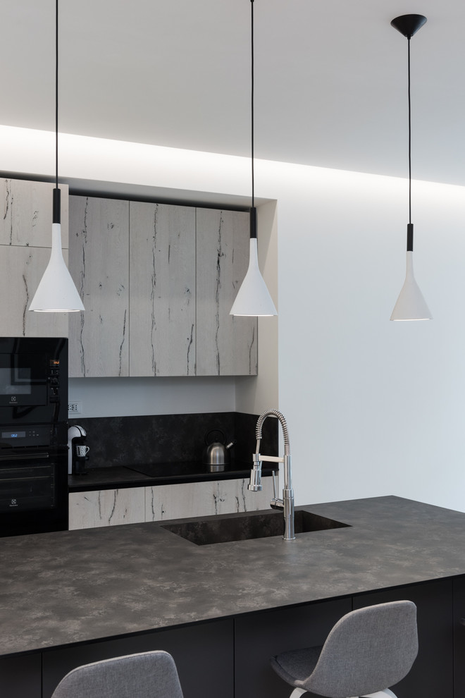 Immagine di una piccola cucina moderna con lavello integrato, paraspruzzi nero, elettrodomestici da incasso, penisola e top grigio
