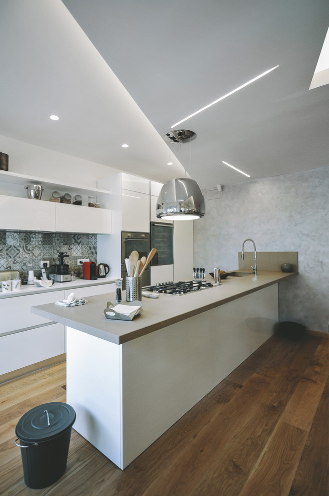 Large contemporary single-wall open plan kitchen in Rome with a submerged sink, flat-panel cabinets, white cabinets, ceramic splashback, stainless steel appliances, medium hardwood flooring and a breakfast bar.