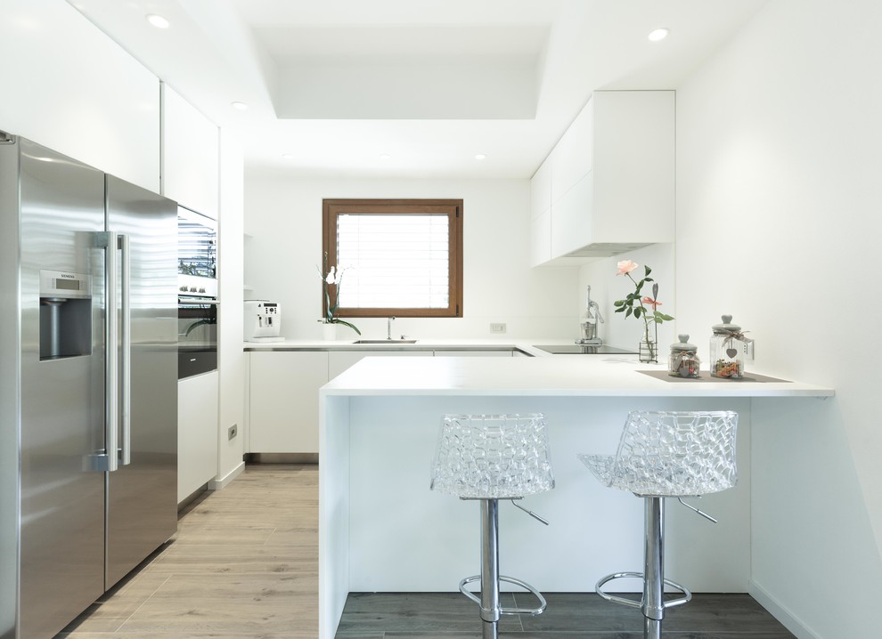 Inspiration for a medium sized contemporary u-shaped enclosed kitchen in Other with flat-panel cabinets, white cabinets, composite countertops, white splashback, window splashback, stainless steel appliances, a breakfast bar, grey floors and light hardwood flooring.
