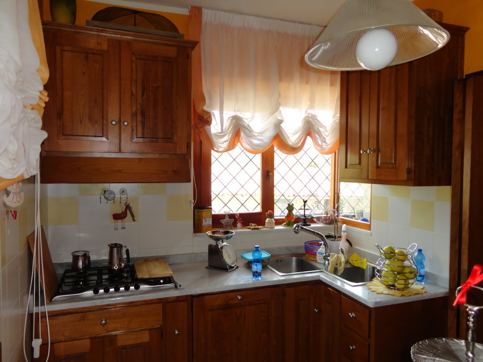 Exempel på ett litet lantligt kök, med en dubbel diskho, luckor med profilerade fronter, skåp i mellenmörkt trä, marmorbänkskiva, gult stänkskydd, stänkskydd i keramik, integrerade vitvaror och klinkergolv i keramik