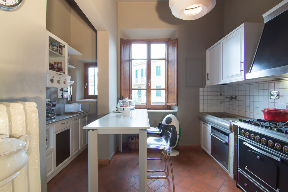 Photo of a small traditional galley enclosed kitchen in Milan with a belfast sink, raised-panel cabinets, white cabinets, quartz worktops, grey splashback, stainless steel appliances, terracotta flooring and an island.