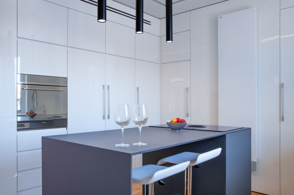 Esempio di una grande cucina design con lavello sottopiano, ante lisce, ante bianche, top in superficie solida, elettrodomestici neri, parquet chiaro e top grigio