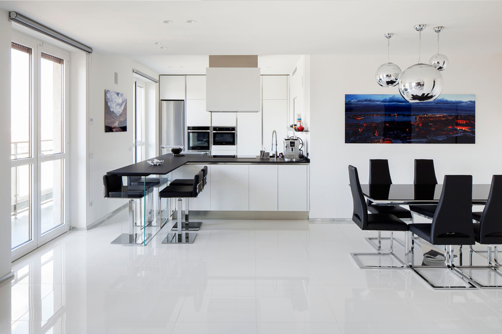 Immagine di una grande cucina abitabile contemporanea con pavimento in gres porcellanato, pavimento bianco, ante lisce, ante bianche, elettrodomestici in acciaio inossidabile, penisola e top nero