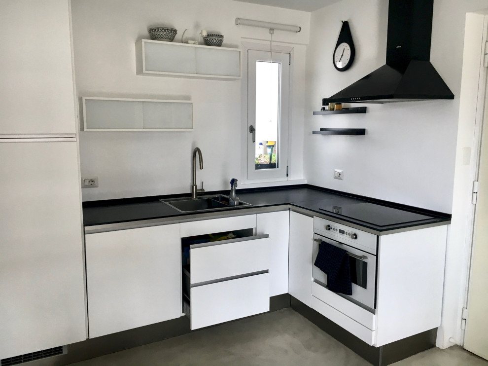 Foto på ett litet skandinaviskt svart kök, med en nedsänkt diskho, vita skåp, laminatbänkskiva, vita vitvaror, betonggolv och grått golv